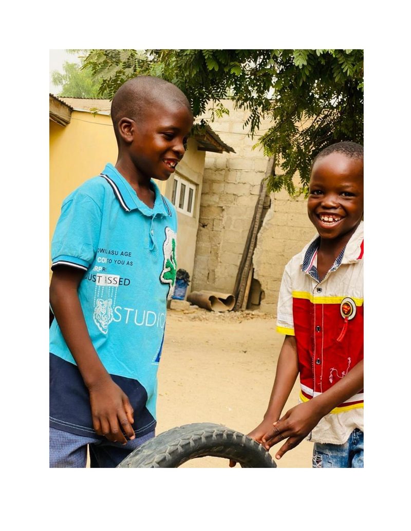 Ahmad and a friend in their neighbourhood rolling a tyre together, both laughing