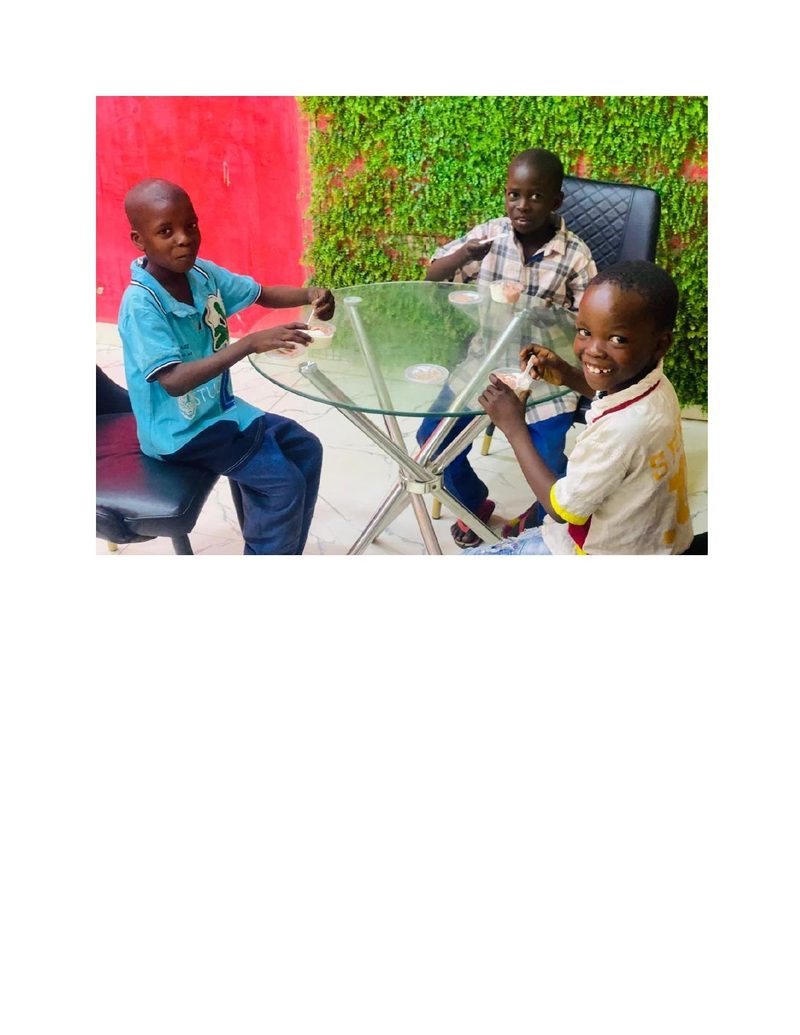 Three boys including Ahmad sitting around a glass table eating ice cream, Ahmad smiling at the camera