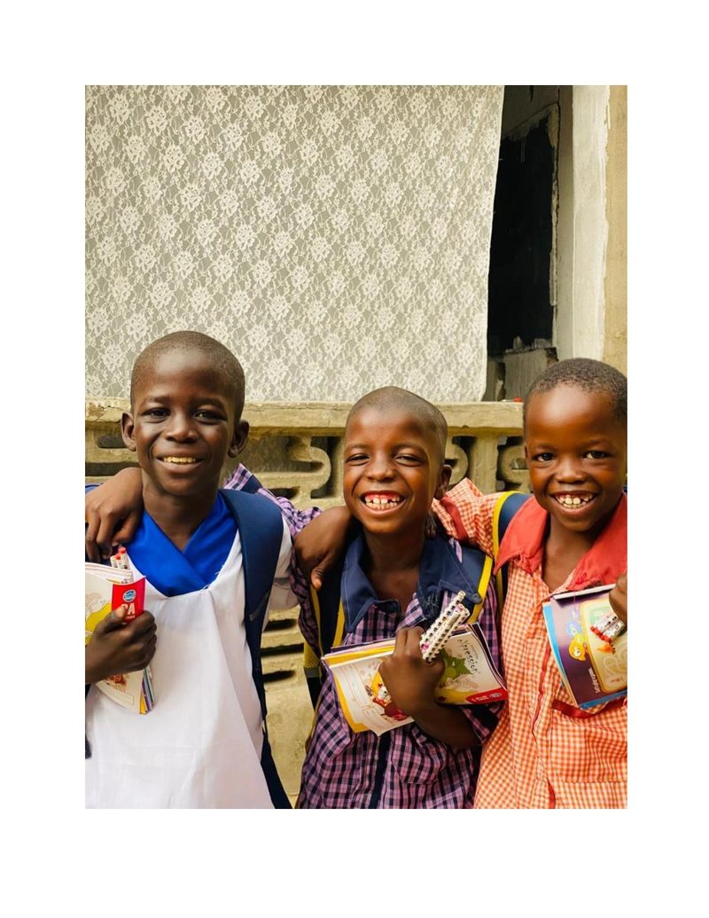 Ahmad and two friends standing with arms around each other holding school supplies and books, all grinning