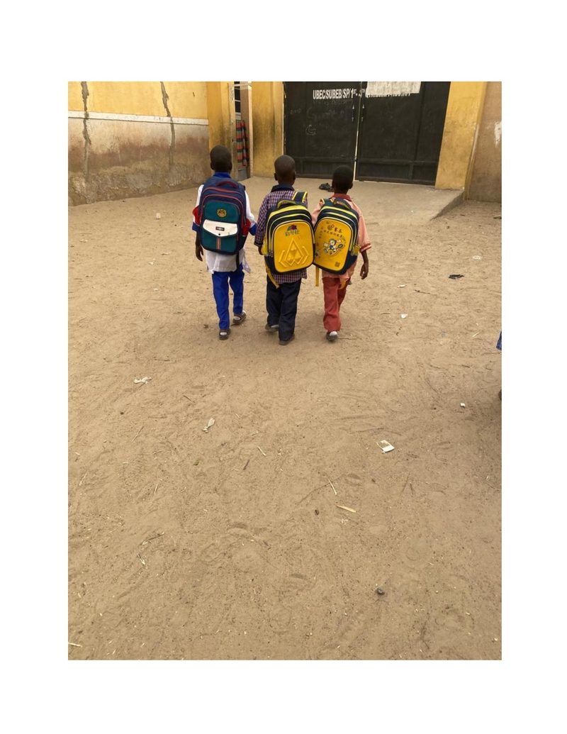Three boys including Mohammed Ali walking toward a school gate with their colourful backpacks
