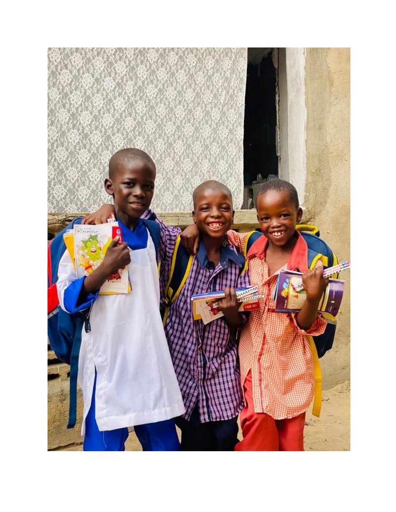 Mohammed Ali and two friends standing together with arms around each other, holding school supplies and grinning