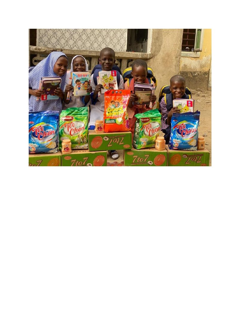 Group of children behind a large pile of donated supplies including books, bags, drinks and detergent