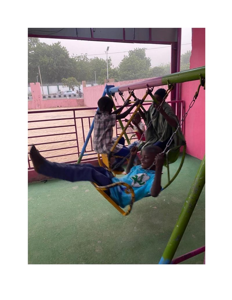 Boys playing on playground swings, Mohammed Ali laid back laughing on one of the swings