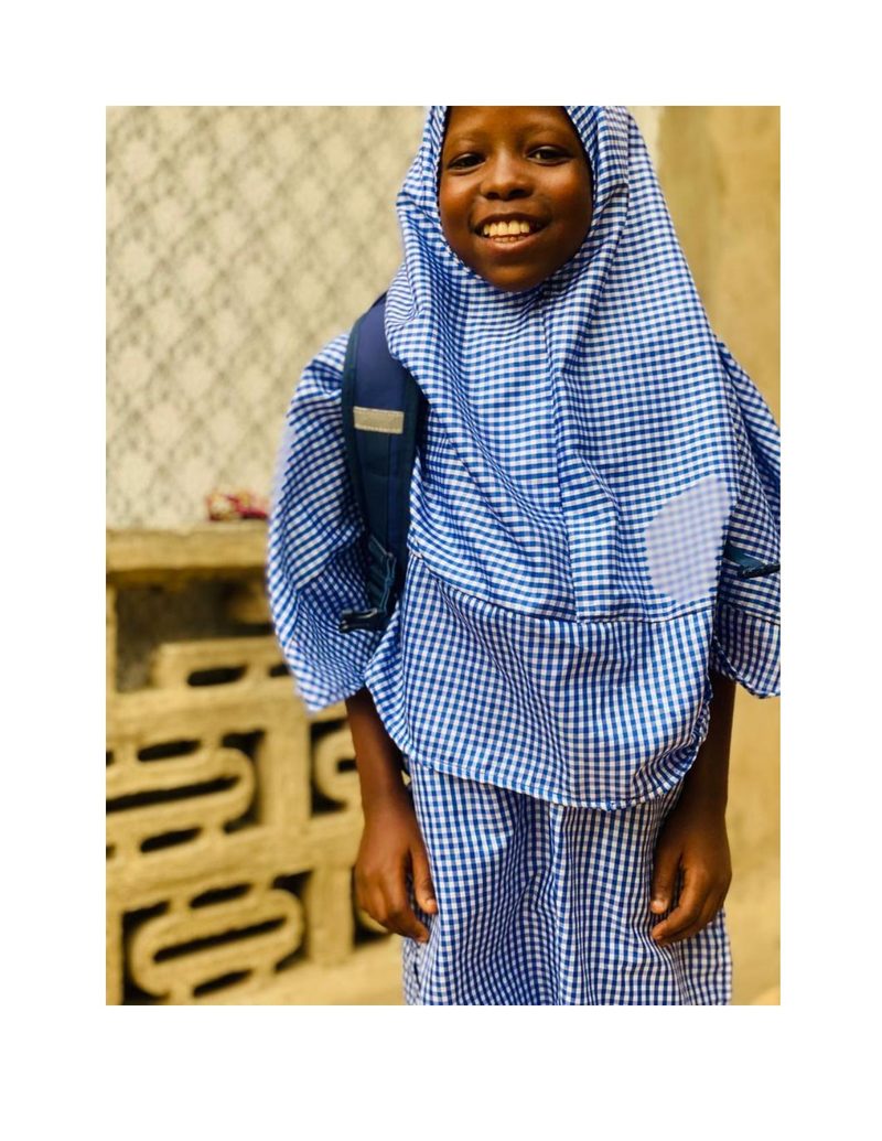 Bilkisu standing tall in her school uniform outside her home