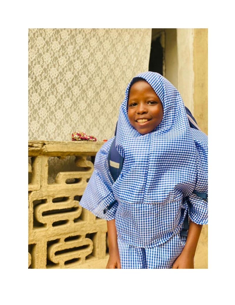 Bilkisu smiling warmly outside her home before school