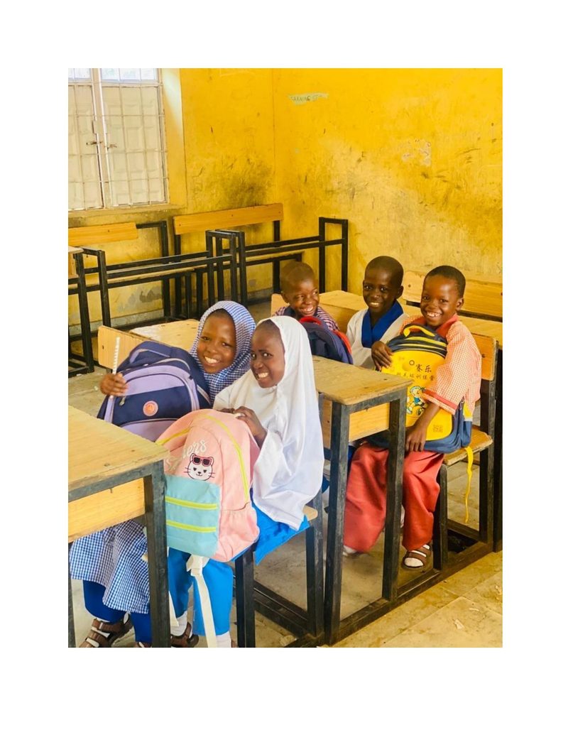 Bilkisu and her classmates sitting at school desks smiling at the camera