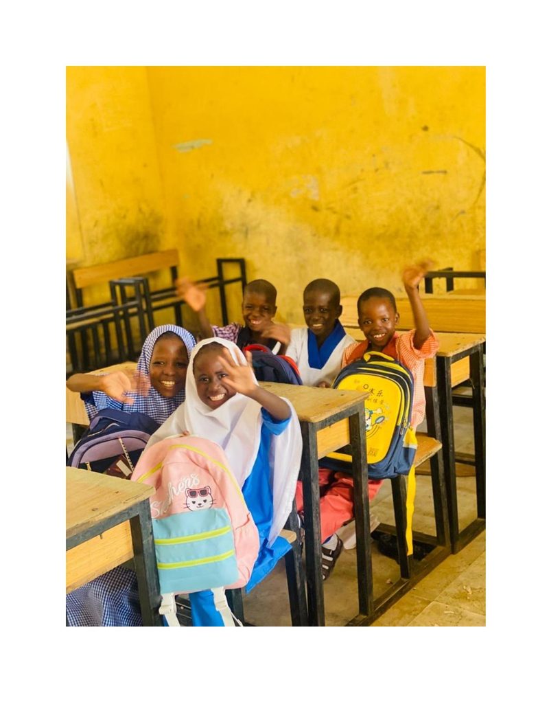 Bilkisu and classmates waving and laughing together in the classroom