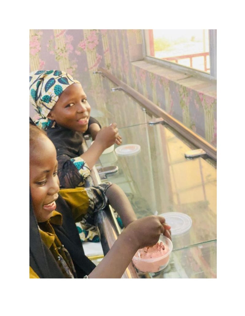 Two girls eating ice cream together at a restaurant table, smiling