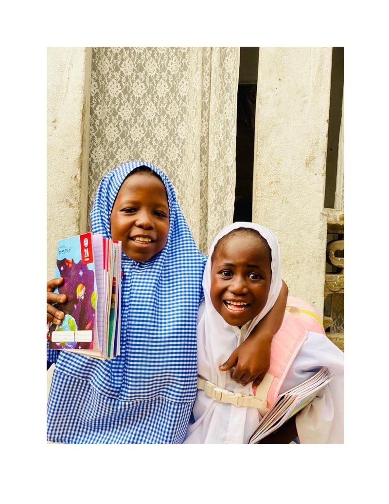 Bilkisu and a friend holding their new books and smiling at the camera