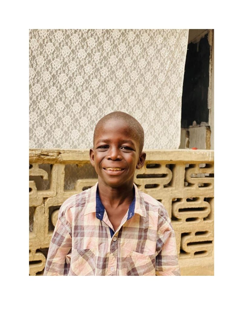 Musa Mohammed in casual clothes before receiving his uniform, smiling outside his home