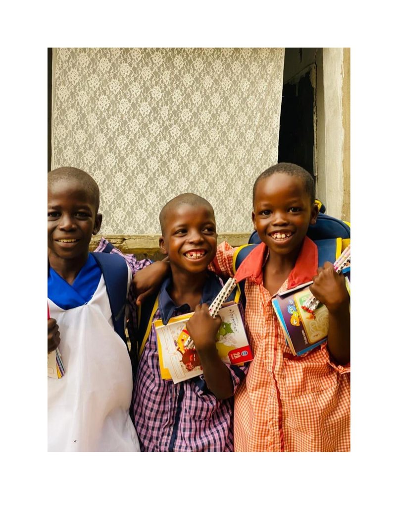 Musa and two friends with arms around each other, holding new school supplies and laughing